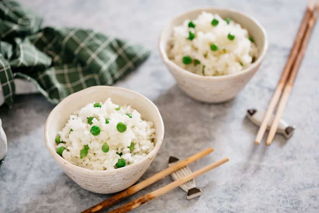 two bowls of green peas and rice with two pairs of chopsticks