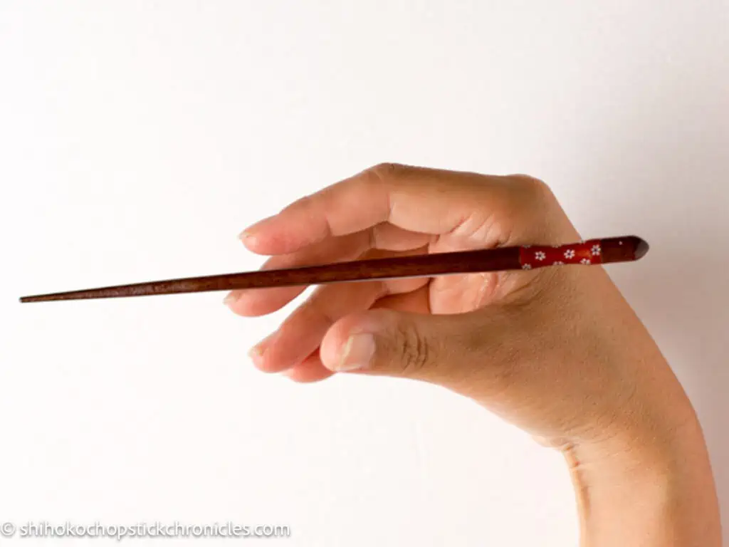 placing one chopstick on between base of thumb and an index finger