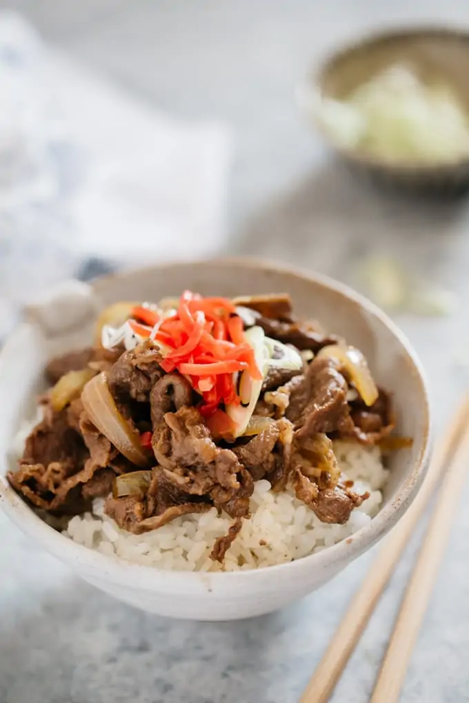 Gyudon served in a Japanese pottery bowl garnished with red pickled ginger on top 