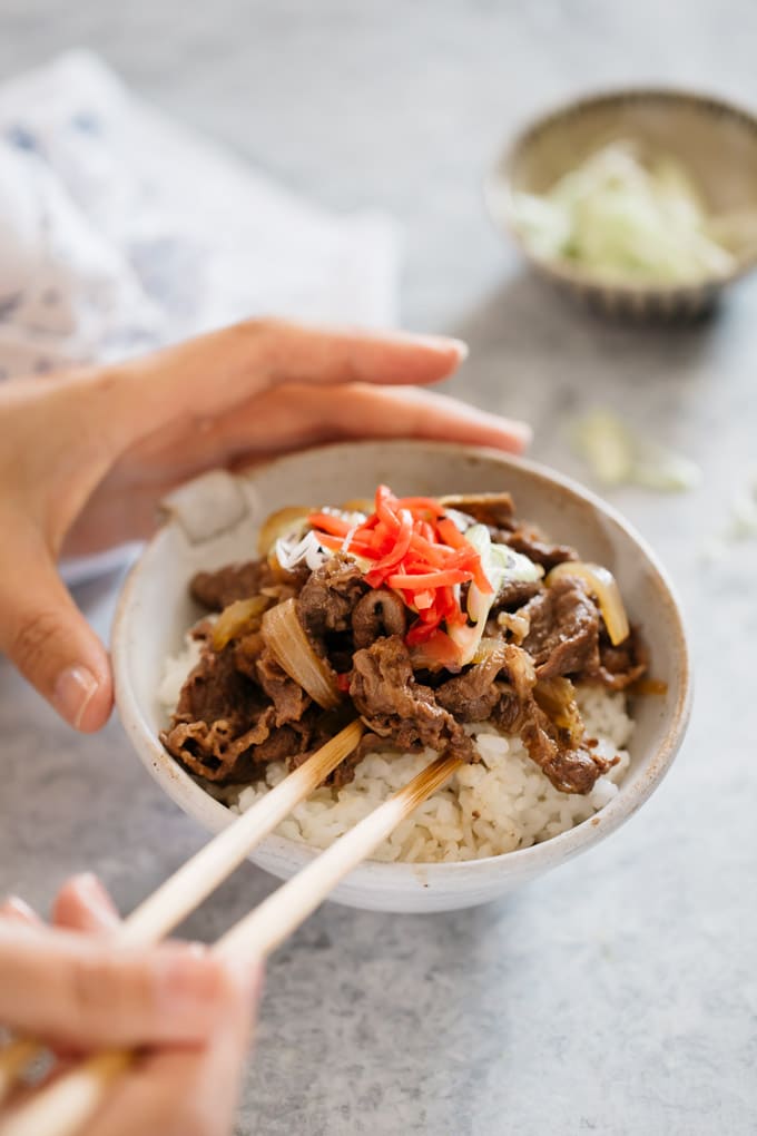 Gyudon served on the rice bowl and a pari fo chopstick digging into the dish.