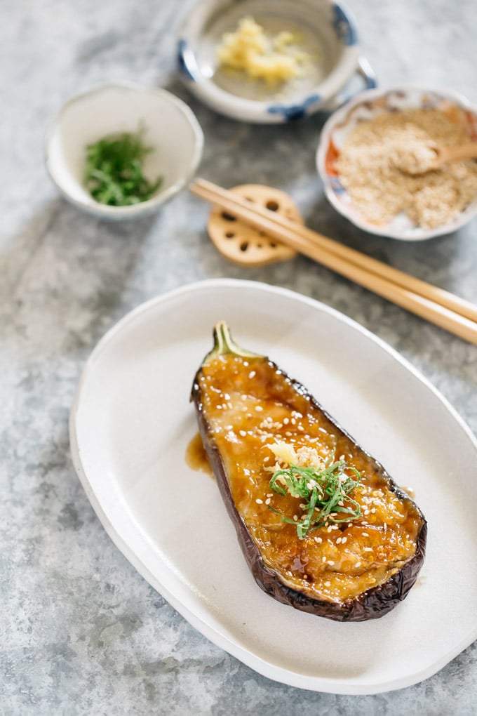 miso eggplant served on an oval shaped plate with three little bowls of garnishes-ginger, shiso leaves and sesame seeds