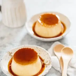 Two Japanese custard pudding served on two Japanese pottery plates with two wooden spoons
