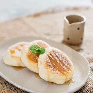 three souffle pancake served on an oval plate dusted with icing sugar and syrup