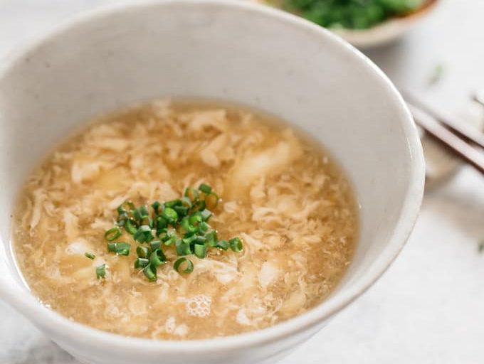 Egg drop soup served in a large Japanese pottery bowl garnished with chopped scallion