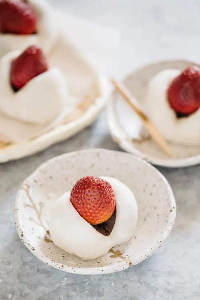 one strawberry mochi on a small plate and in the background too.