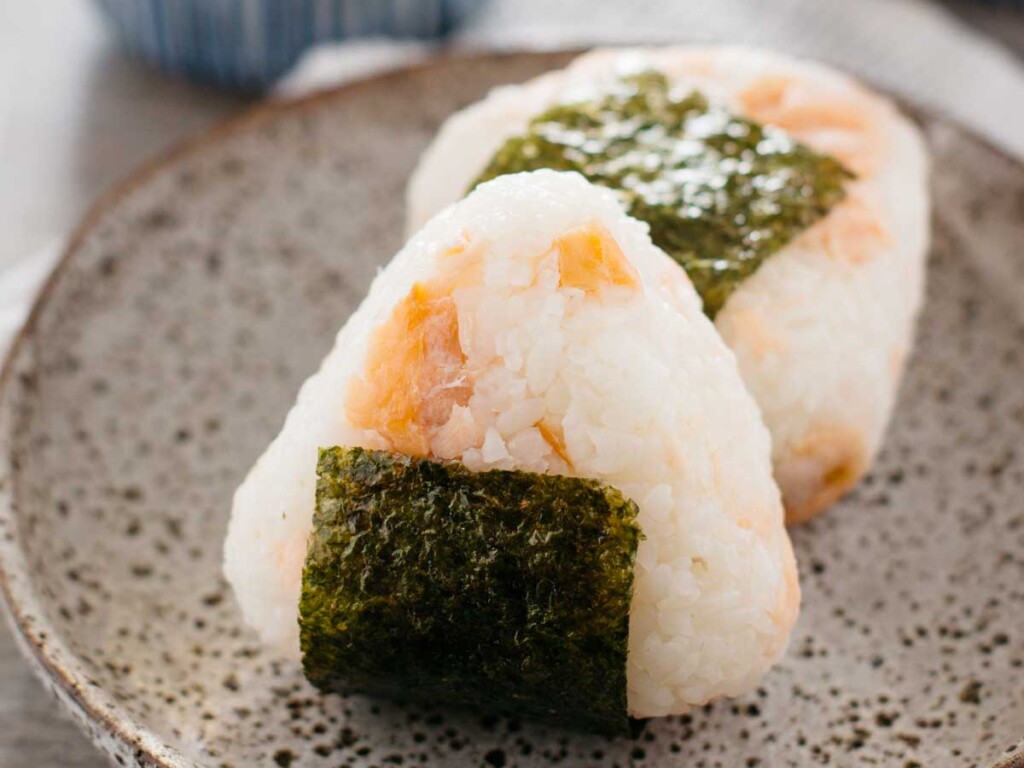 two salted salmon onigiri fillings on a plate with a cup of green tea