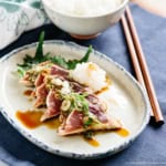 Katsuo tataki slices served on a oval plate with grated daikon and chopped scallions