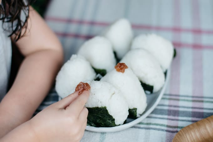 a little girl's hand putting umeboshi paste on to a top of onigiri rice ball