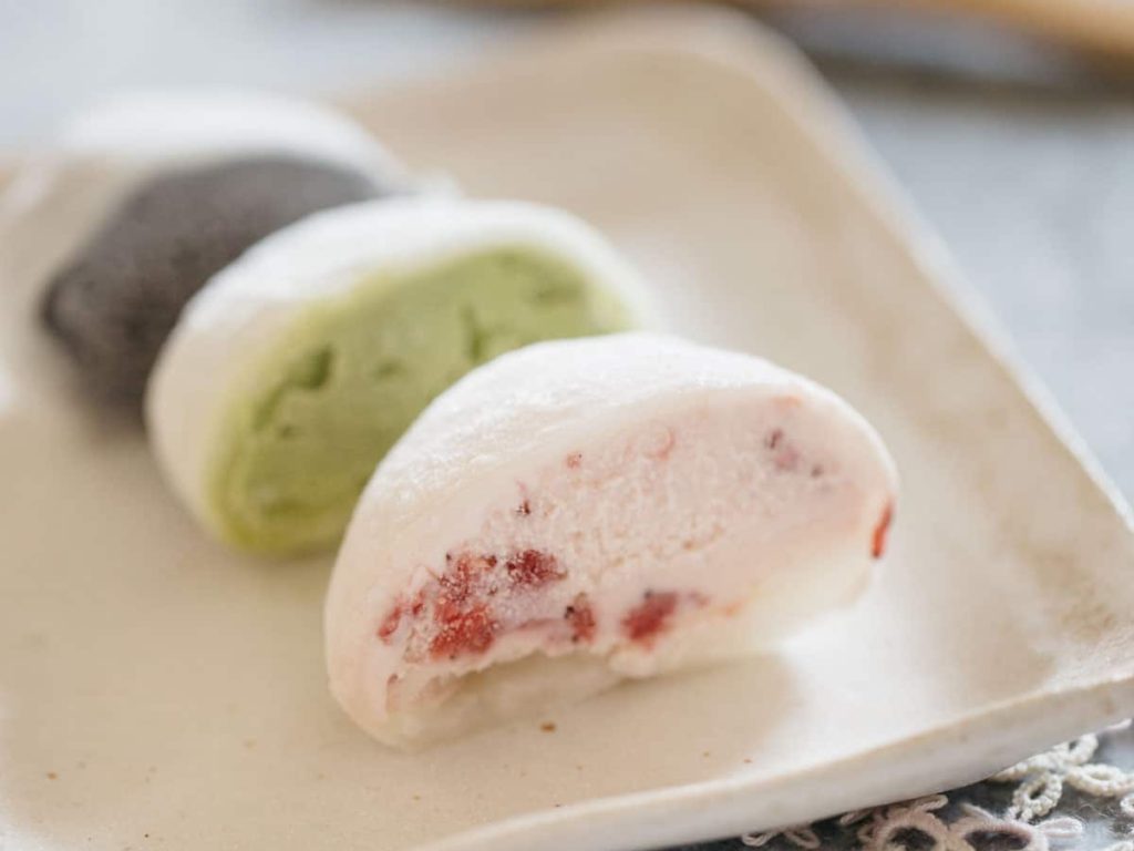1/2 of strawberry, matcha, and black sesame flavour mochi ice served on square shaped plate with a wooden folk