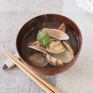 Japanese clear soup with manila clams is served in a wooden bowl with a pair of chopsticks