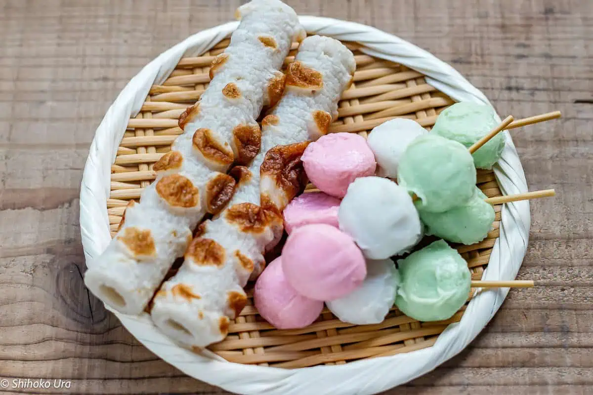two chikuwa and 4 fish cake balls on skewers on a bamboo tray