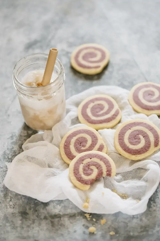 6 pinwheel cookies with purple sweet potato are scattered on with a glass of iced coffee