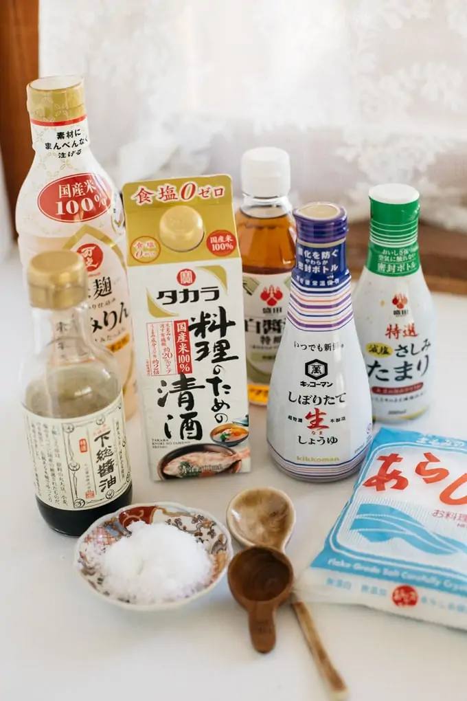 a bottle of mirin, 4 bottles of different types of soy sauce, a carton of sake, and a packet of salt