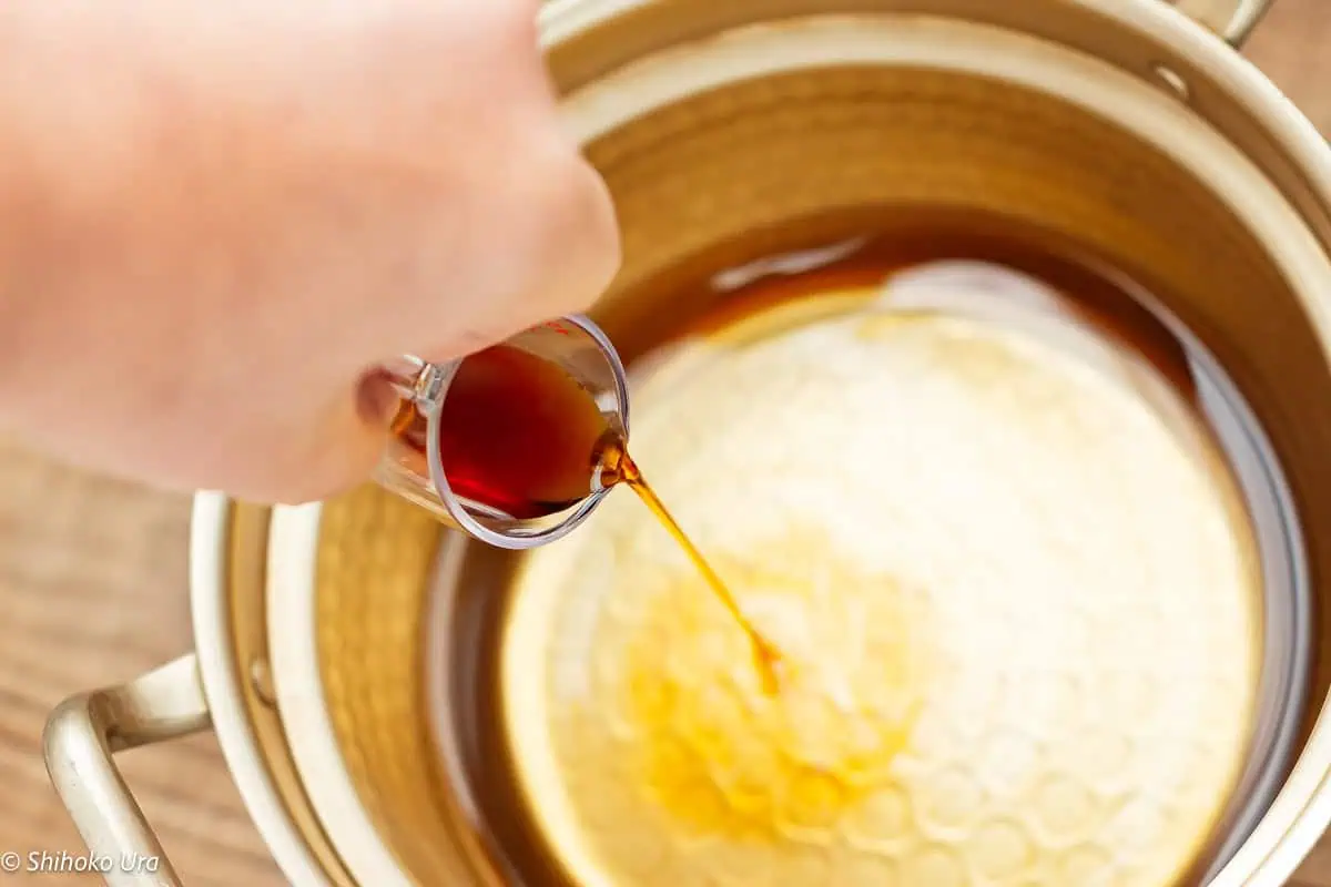 dashi in a cooking pot and pouring soy sauce in
