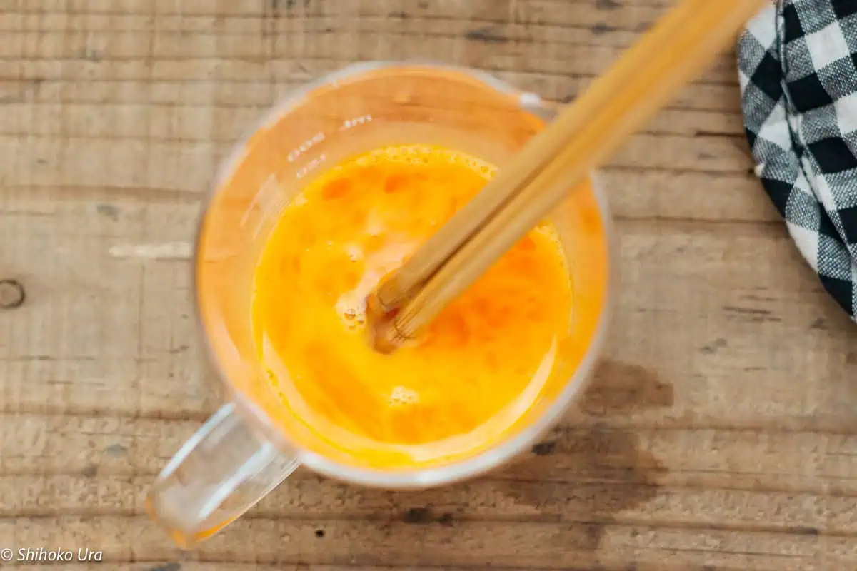 beating egg in a measuring cup with chopsticks