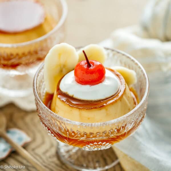 Purin (Japanese custard pudding) with banana slices and cherry on top in a glass dish.