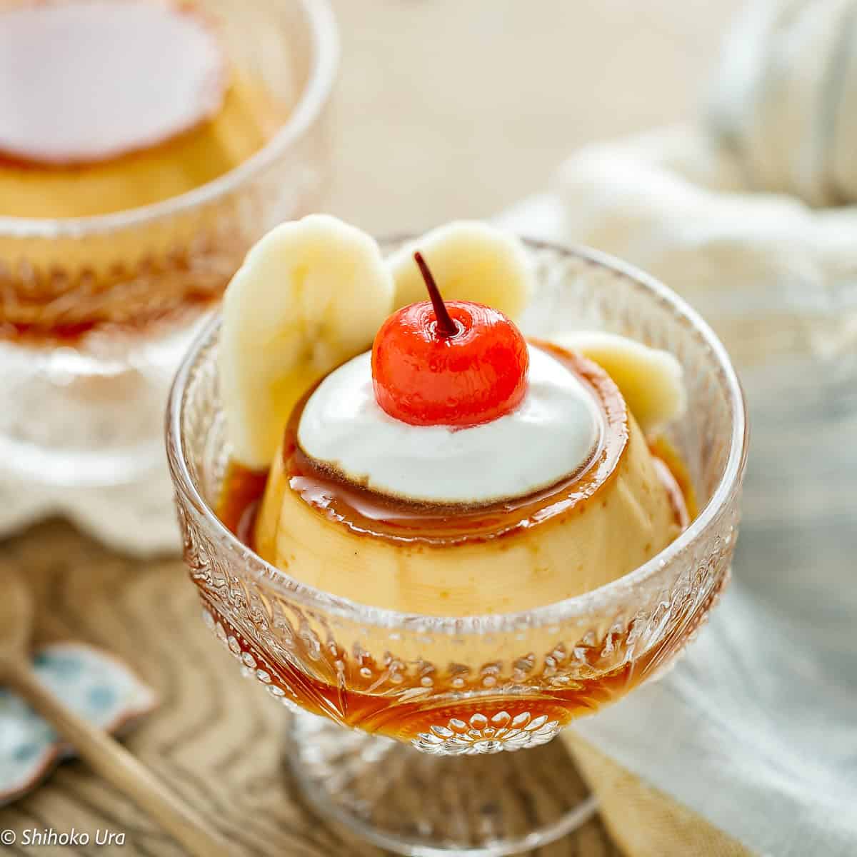 Purin (Japanese custard pudding) with banana slices and cherry on top in a glass dish.