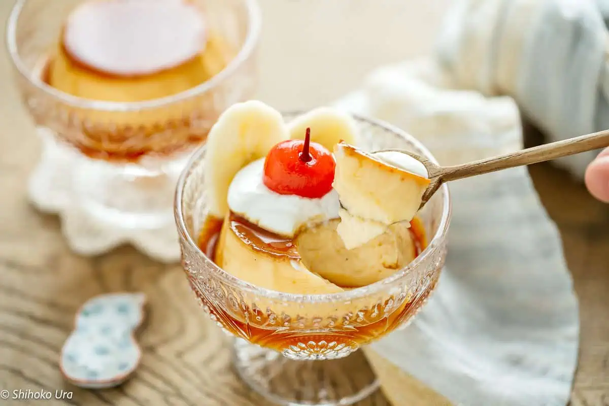 Delicious Japanese custard pudding topped with whipped cream and cherry in a glass bowl.