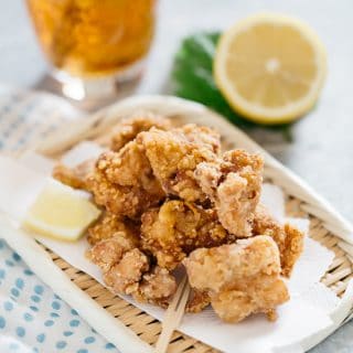 Karaage served on a bamboo tray with drink in the background with half lemon