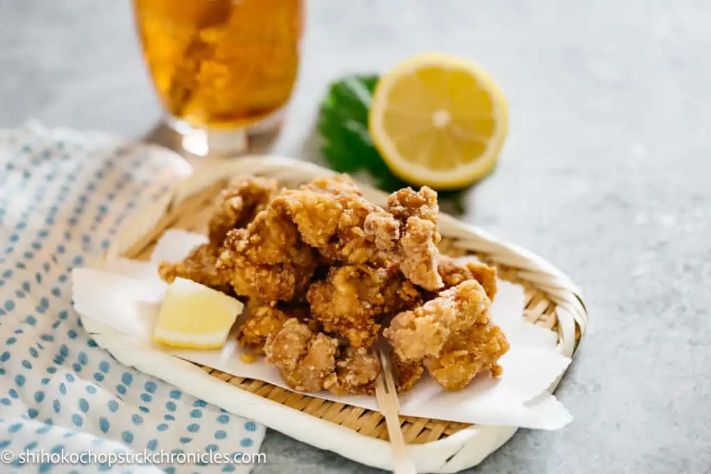 karaage chicken on a bamboo tray with half cut lemon and a glass of drink