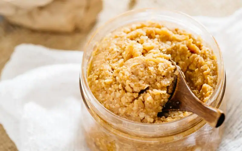 homemade miso paste in a clear container with a small wooden spoon
