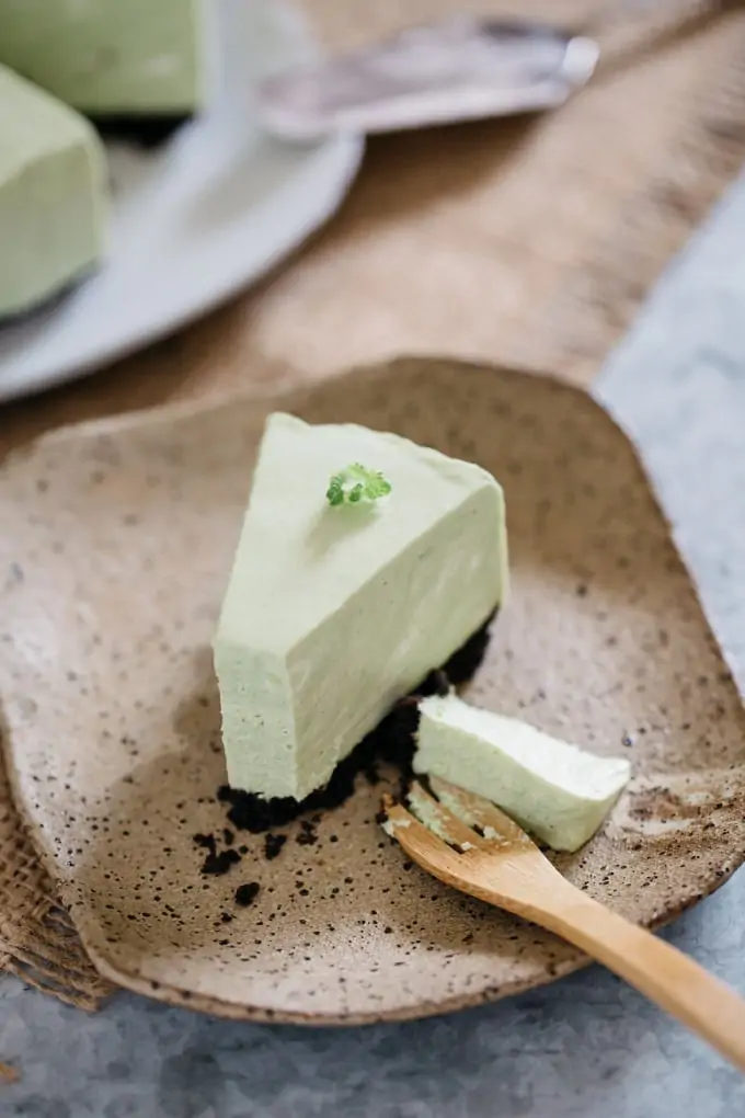 A piece of no bake cheesecake matcha oreo crust served on a square plate with a bamboo folk