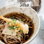 Toshikoshi soba served in a noodle bowl with a prawn tempura and kamaboko fish cake slices with soup
