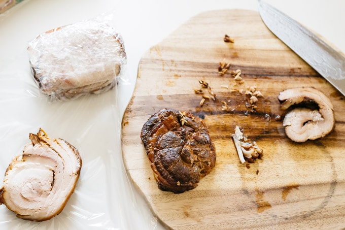 Chashu slices on a chopping board, some are wrapped in cling wrap. 