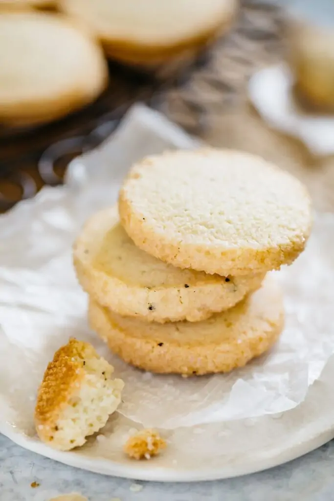 Three butter cookie stacked on a round plate with some crumbs