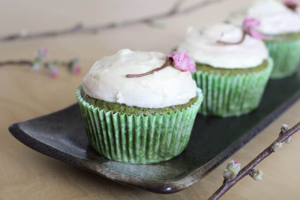 Three matcha cupcakes with white frosting and salted cherry blossom flower 