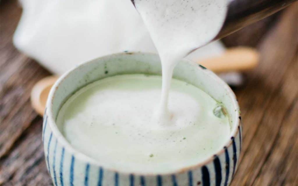 matcha latte being made. Flossed milk pouring into the matcha bowl 