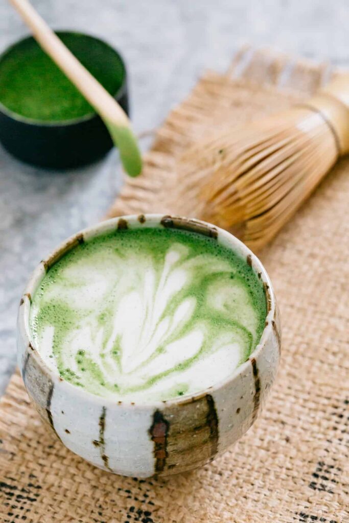 Matcha Latte served with latte art. A bamboo whisk in background.