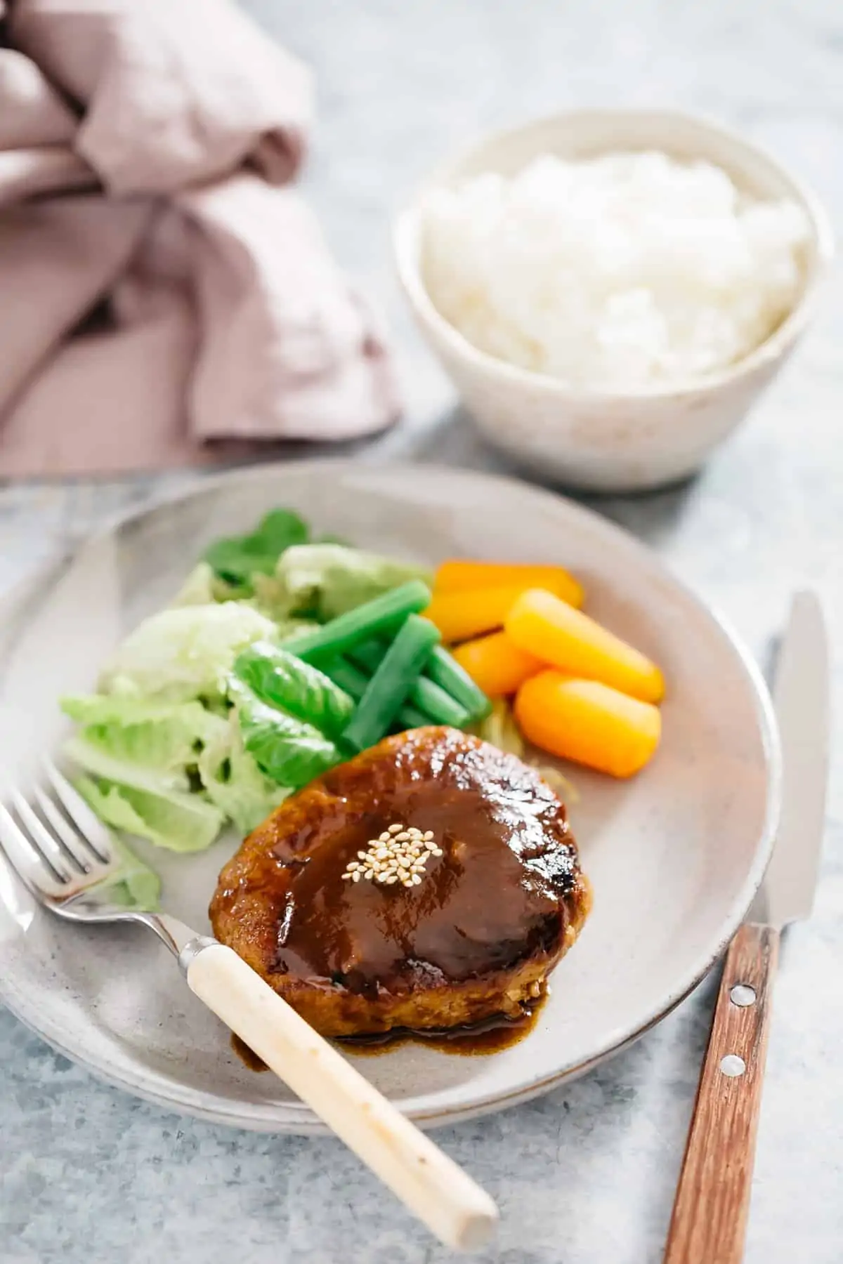 A Japanese hamburger steak served on a round plate with green salad veggies and carrots and green beans.