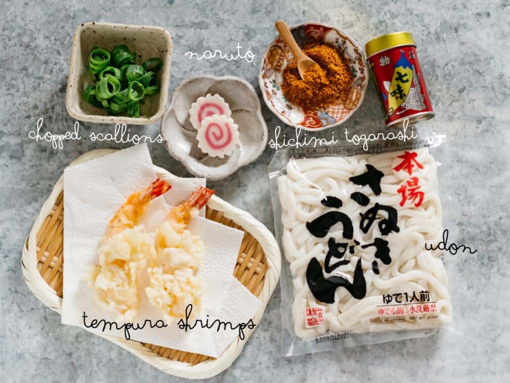 two tempura shrimp, one udon noodle packet, two slices of Naruto fish cakes, shichimi togarashi and chopped scallions