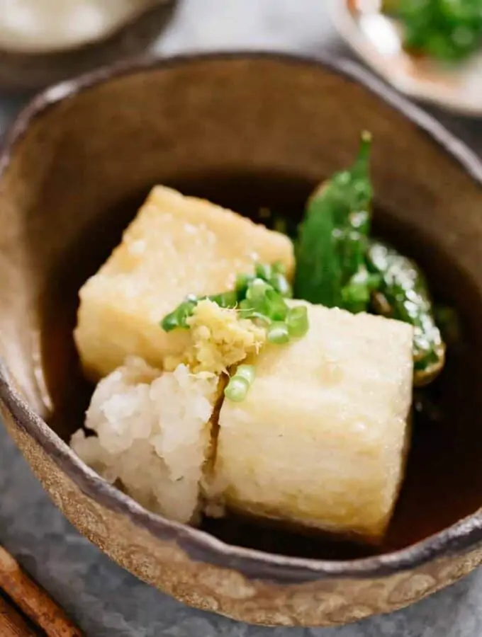 Two Agedashi tofu served in a oval bowl with garnishes and tsuyu