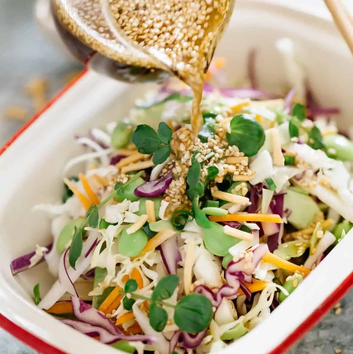 Asian Slaw in a rectangle dish. The sesame soy dressing being pored over.