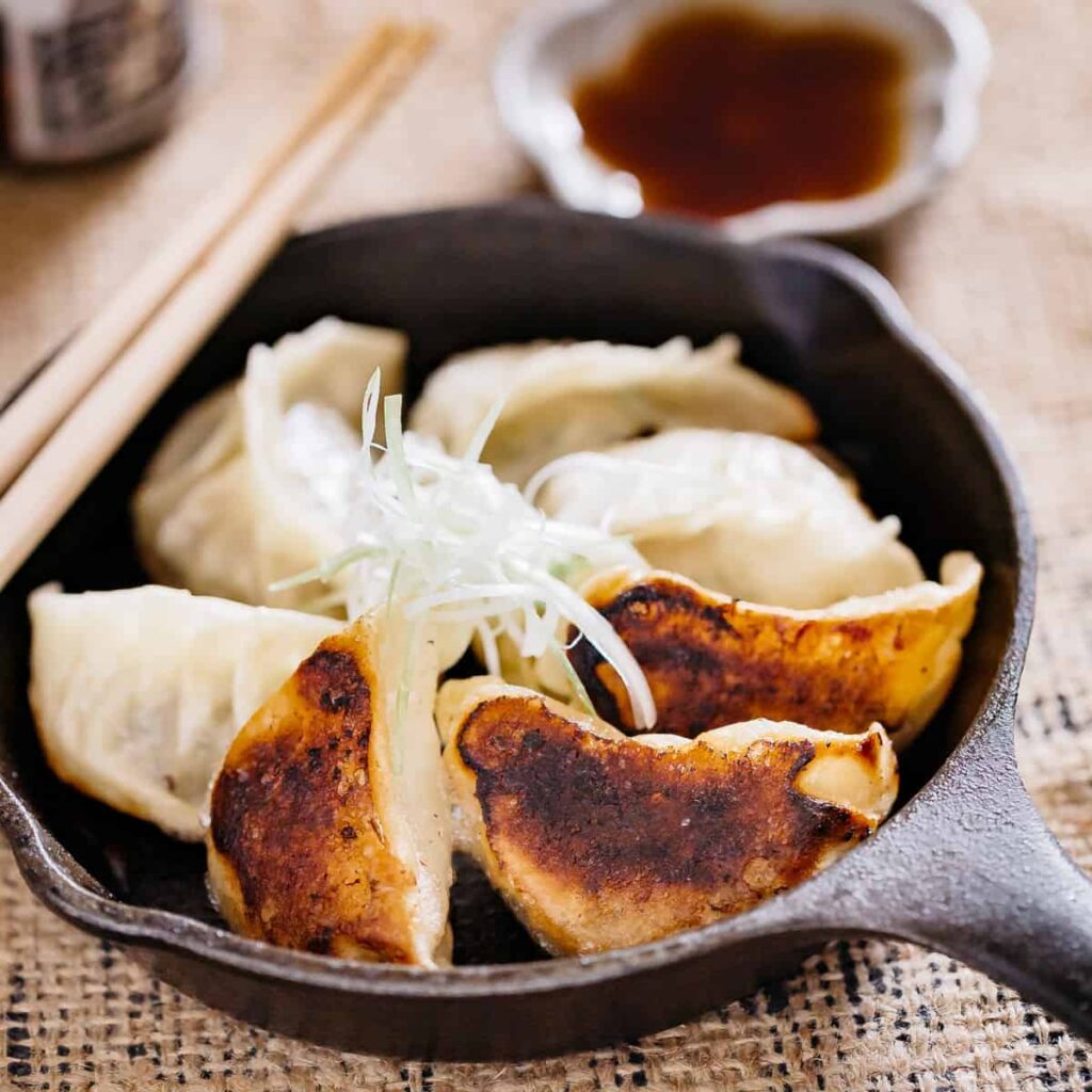 6 gyoza pan fried in a cast iron skillet, three of them showing blackened bottom