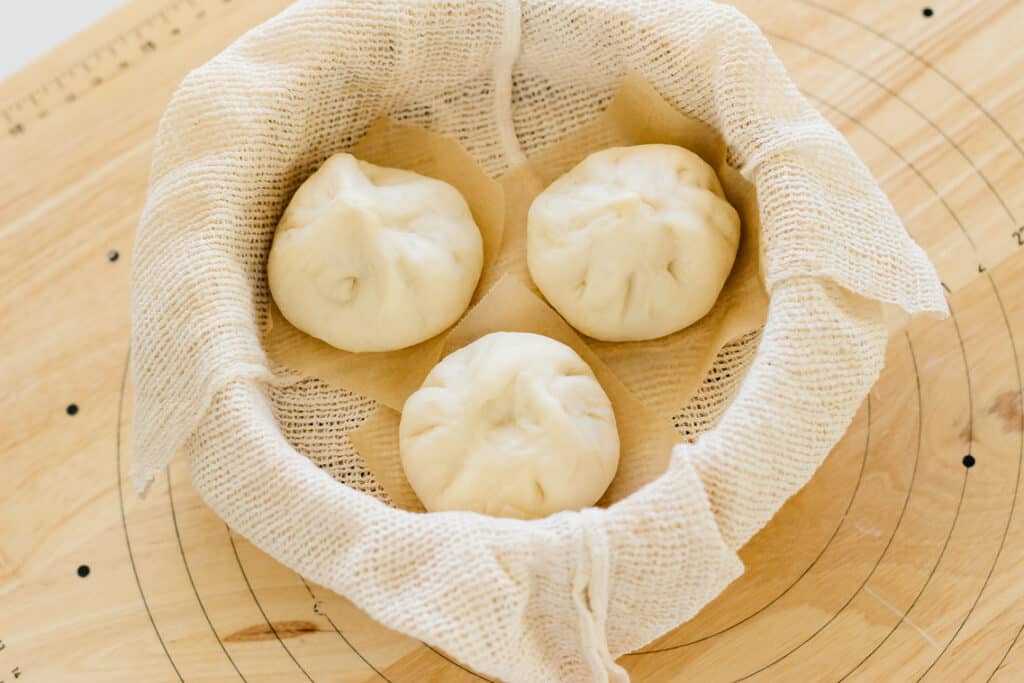 three pork buns before steaming in a bamboo steamer