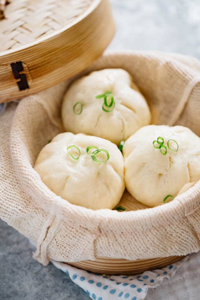 three steamed pork buns served in a bamboo steamer