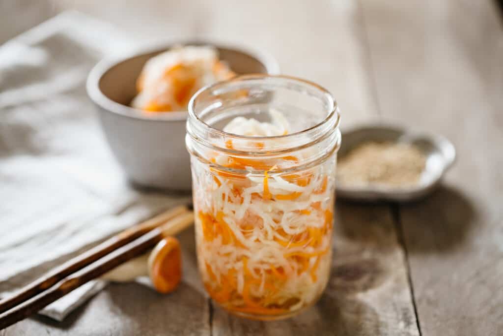 pickled daikon and carrot in a preserving jar, served in a small bowl in the background