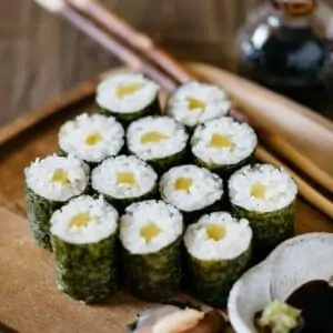 12 pieces of oshinko roll served on a wooden plate with a small bowl of soy sauce with wasabi