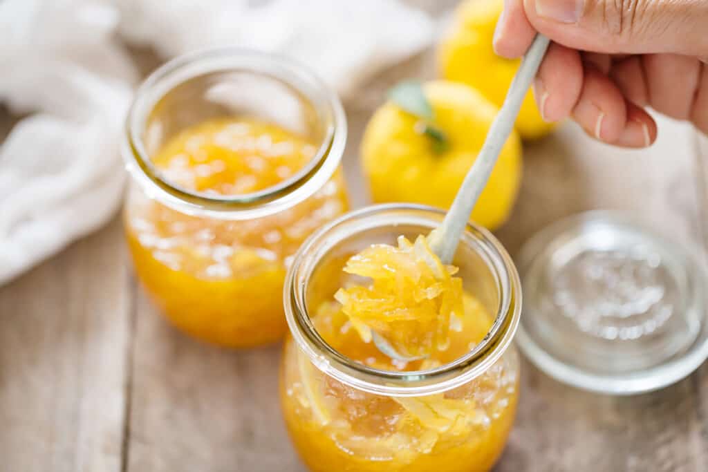 two preserving jars of yuzu marmalade with a spoon taking out some