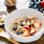 Brown rice and quinoa porridge served in a white bowl with berries and almond slices topped