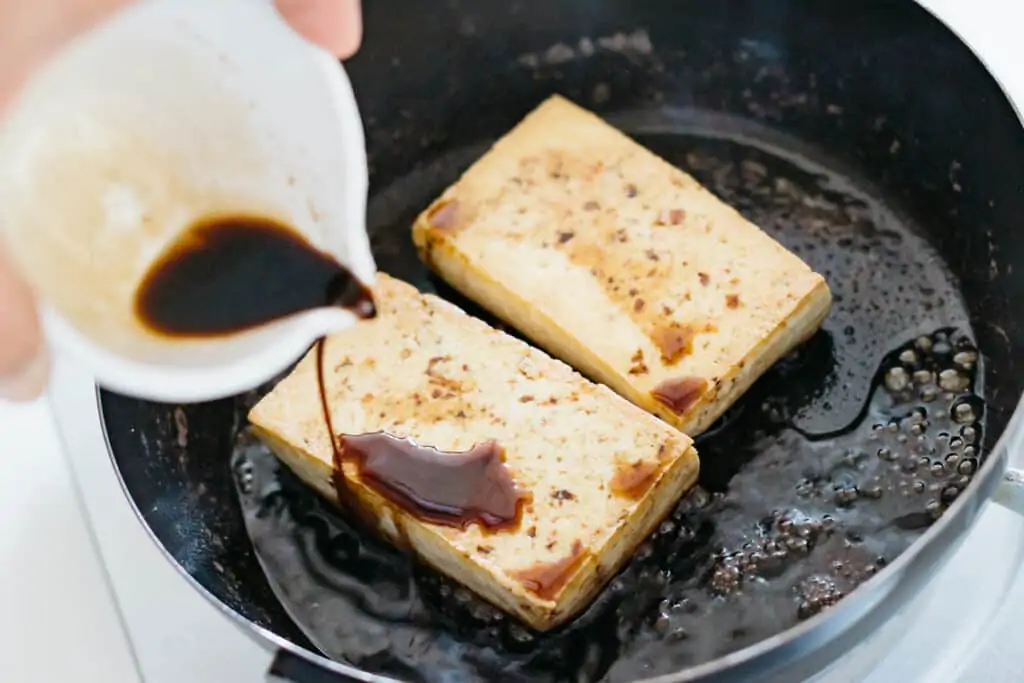 pouring soy sauce base sauce onto fried tofu in a frying pan
