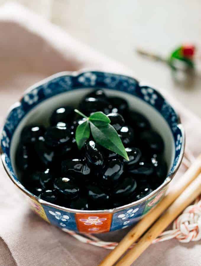 Sweetened black soybeans served in a small bowl with a pair of chopsticks