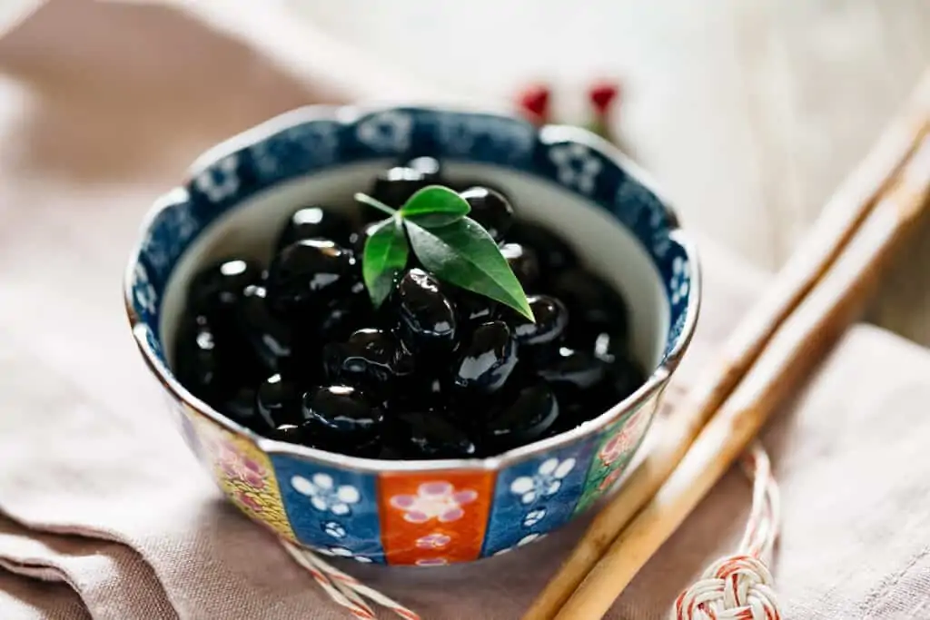 Kuromame simmered black soy beans served in a small shallow bowl.