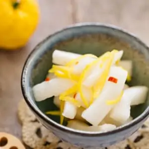 Pickled daikon with yuzu served in a small bowl with a yuzu fruit in background