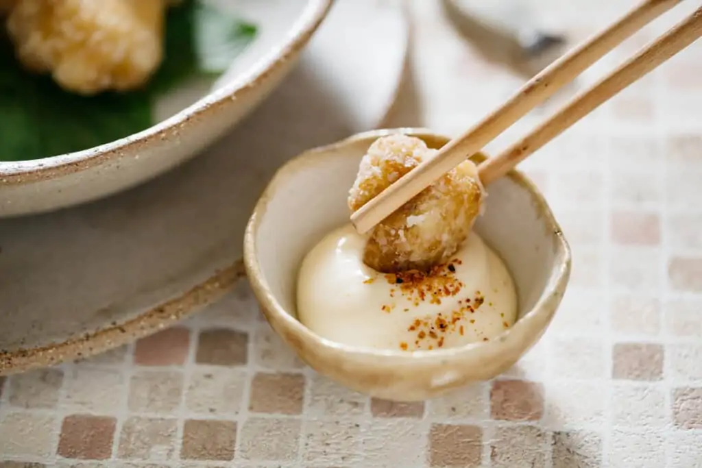 a piece of fried cauliflower dipped into a small bowl of mayonnaise