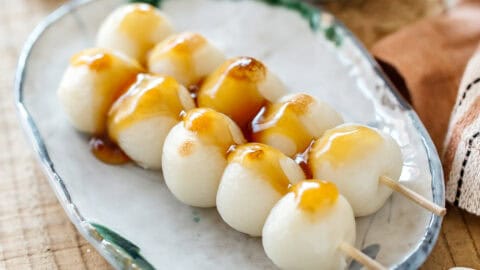 2 skewers of mitarashi dango on an oval plate with mitarashi sauce drizzling