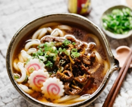nikuudon is served in a serving noodle bowl with three naruto